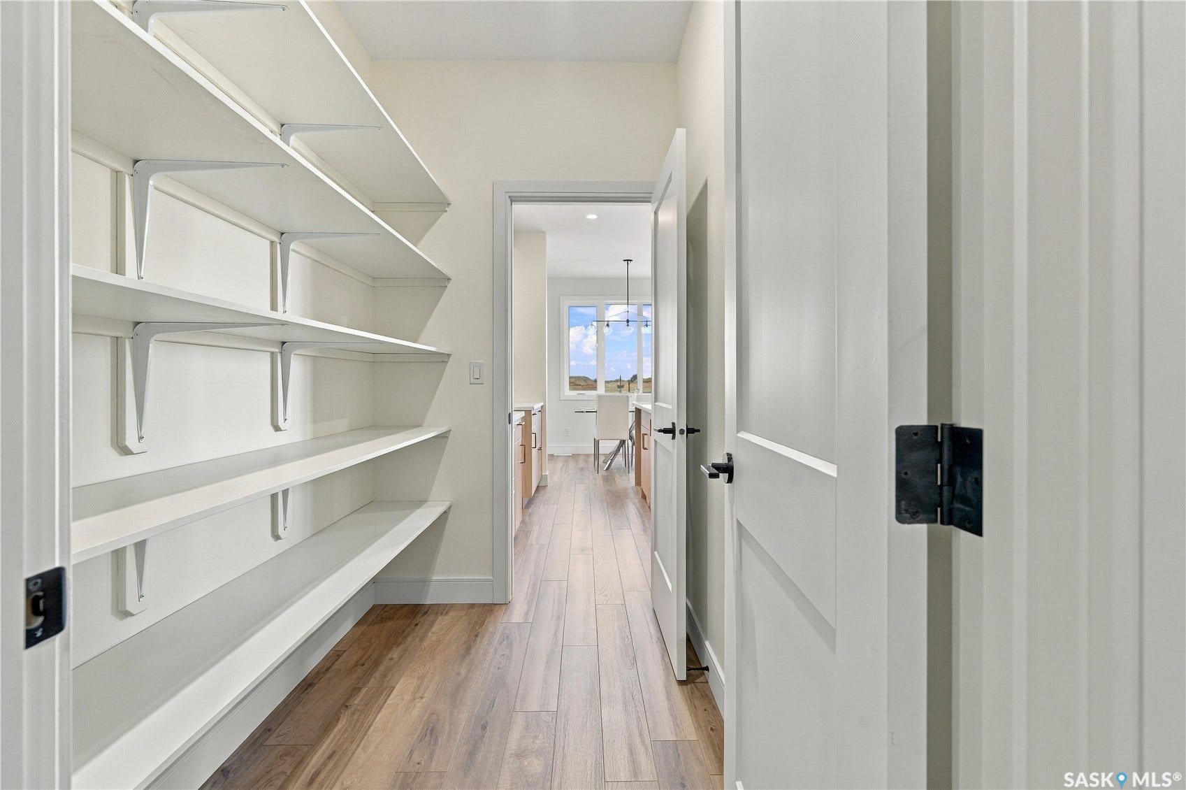 Hallway pantry with extensive built-in shelving, wood-finish flooring, and white paneled doors with matte black hardware