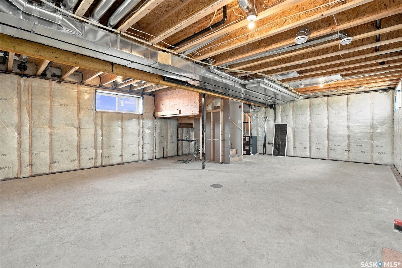 Unfinished lower level with concrete flooring, exposed ceiling joists, and a window well