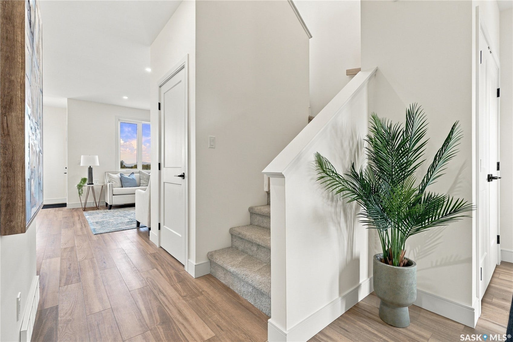 Wood-finish flooring, white walls, recessed lighting, white doors with dark hardware, and a carpeted staircase