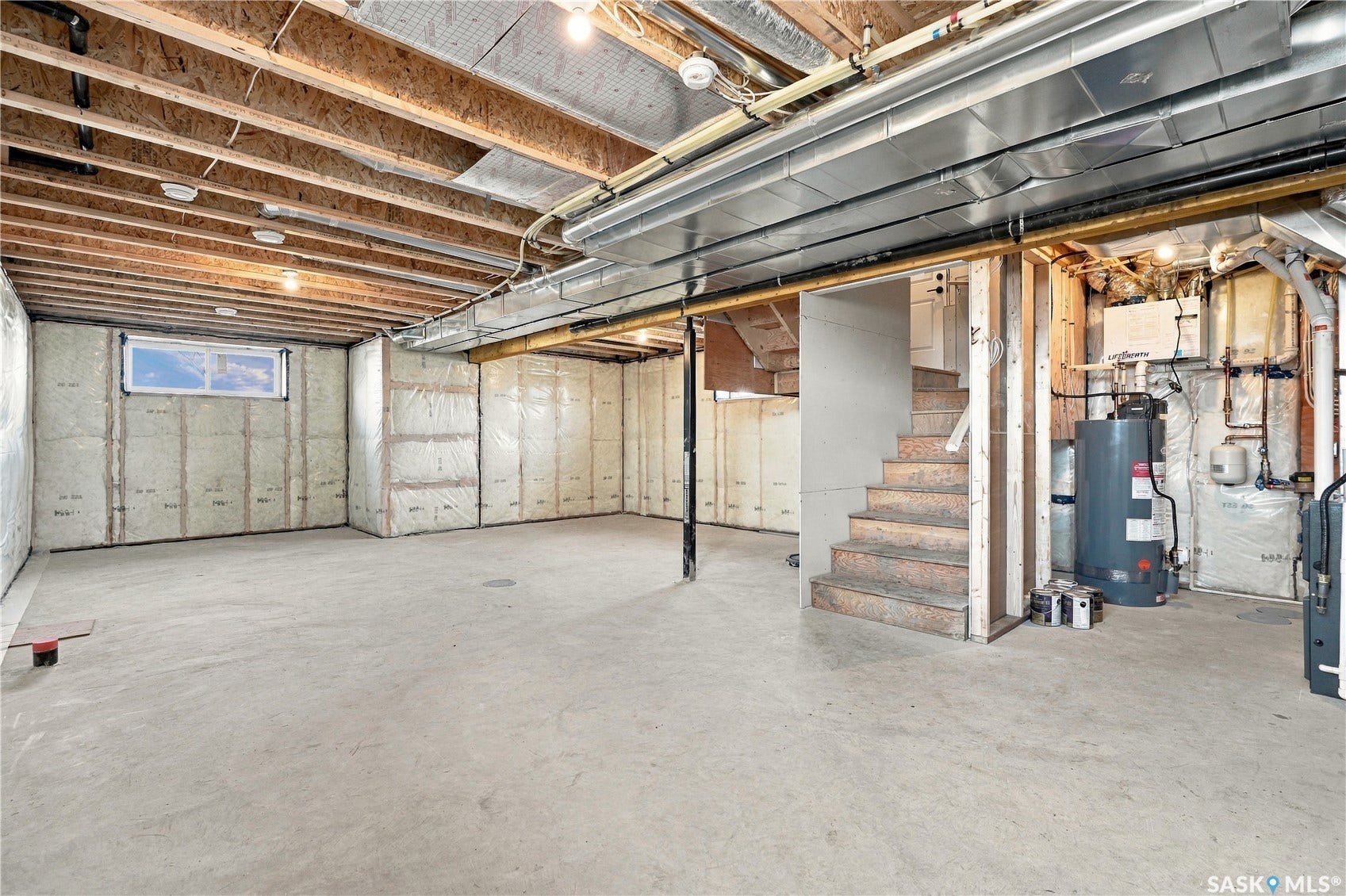 Expansive unfinished basement featuring concrete flooring, exposed ceiling joists, insulated walls, a single window, and a utility area