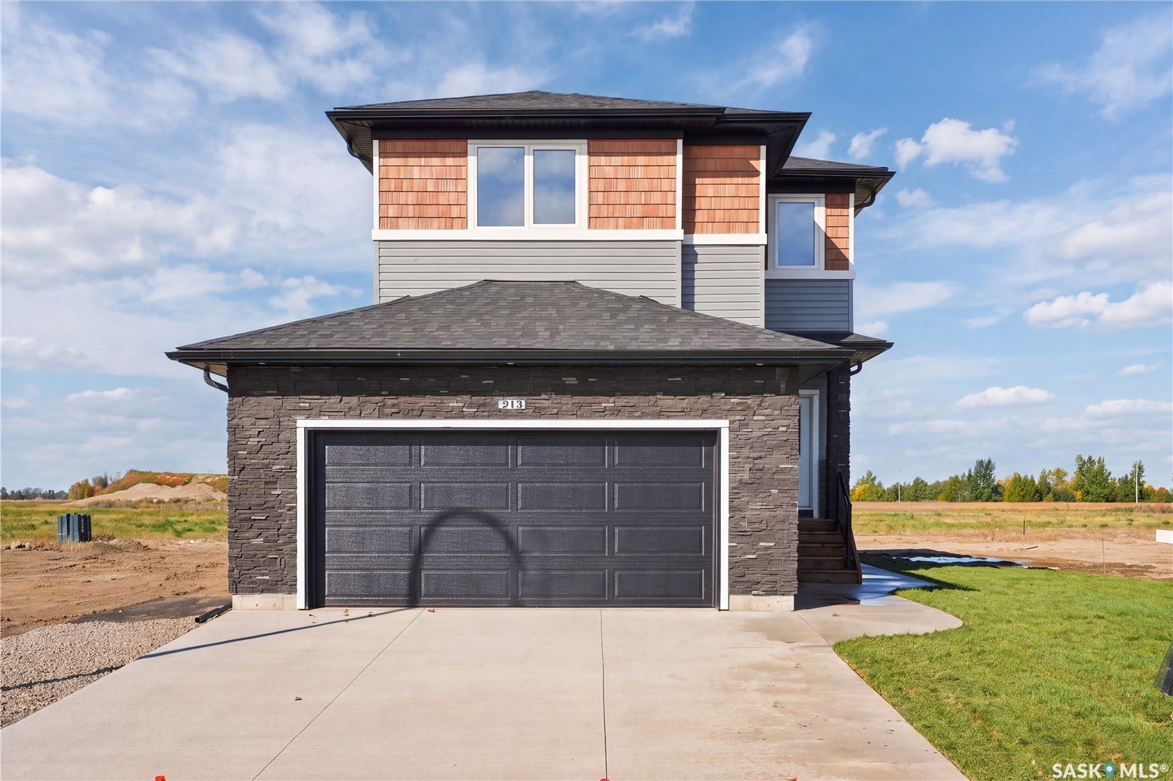 Multi-level exterior featuring a dark grey garage door, stone facade, horizontal siding, and cedar shake shingles