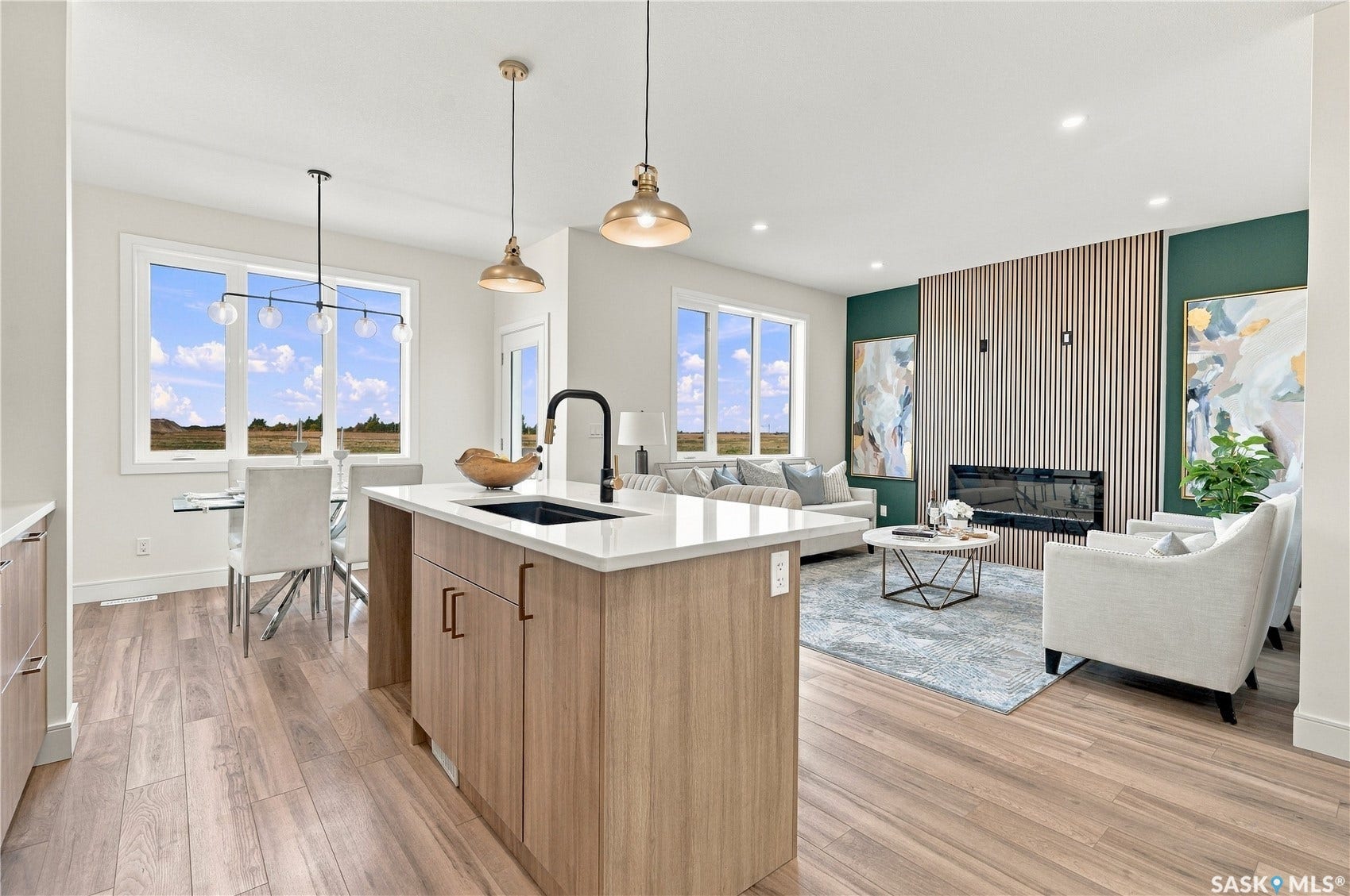 Open-concept living area featuring wood-finish flooring, a kitchen island with a sink and white countertop, and a built-in fireplace with a vertical slat wall accent