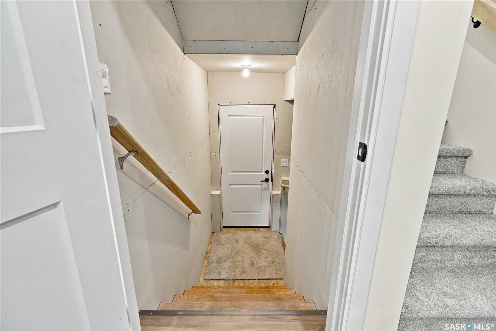 Carpeted stairway with a wooden handrail, white paneled doors, and ceiling-mounted lighting