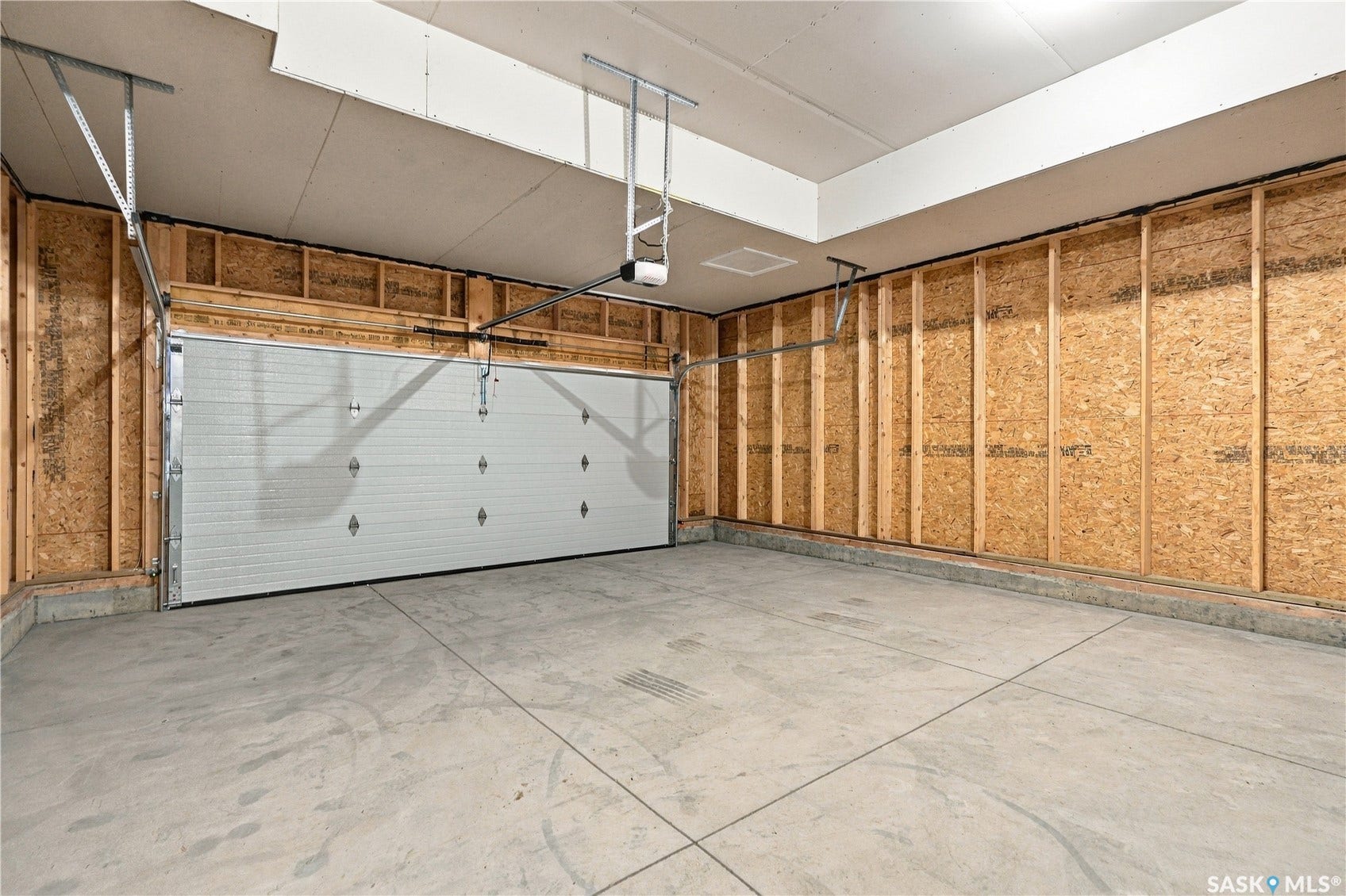 Spacious garage featuring a concrete floor, exposed wood framing, and a white paneled garage door