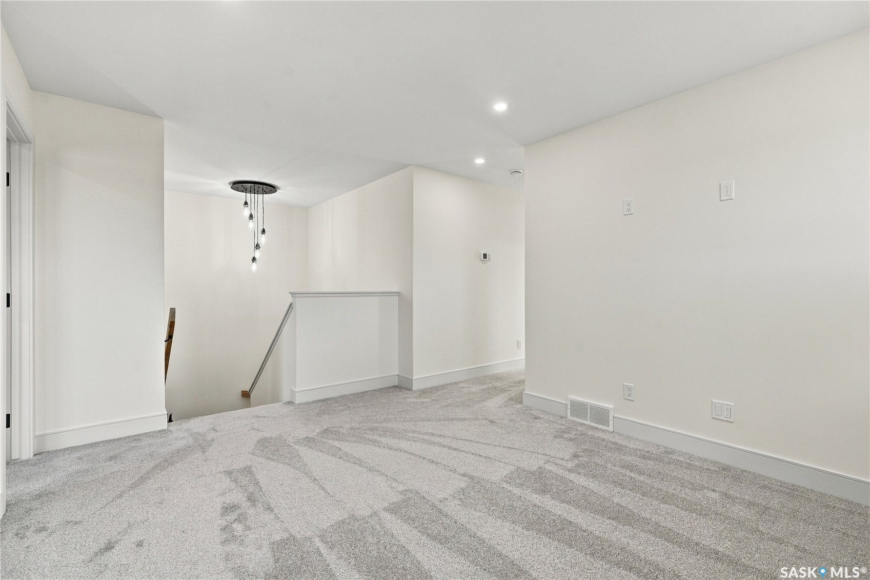 Expansive carpeted area with recessed lighting, a contemporary chandelier, and a white railing