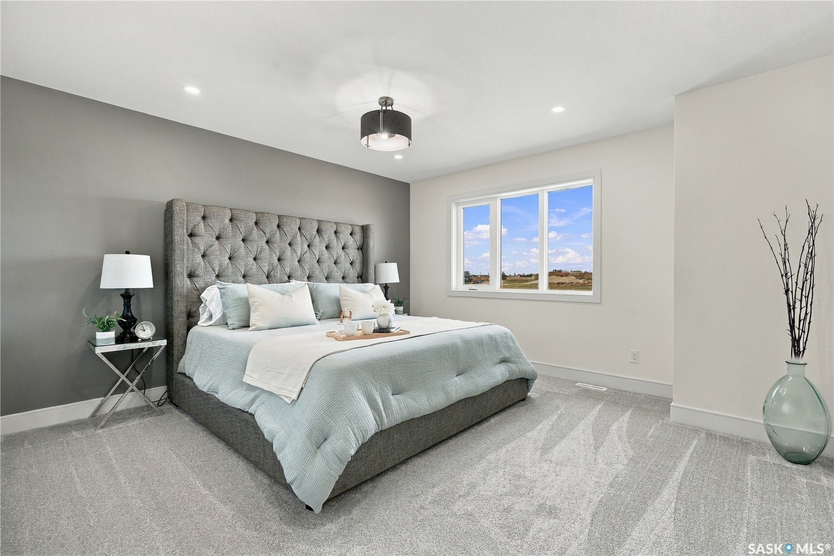 Recessed lighting, large window with expansive outdoor scenery, modern ceiling fixture, upholstered headboard, and light-toned carpeting