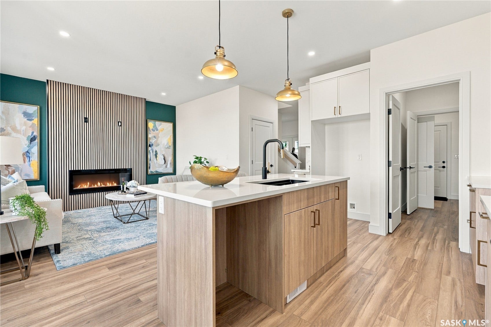 Wood-finish flooring throughout, modern kitchen island with integrated sink, white upper cabinetry, linear electric fireplace, and recessed lighting