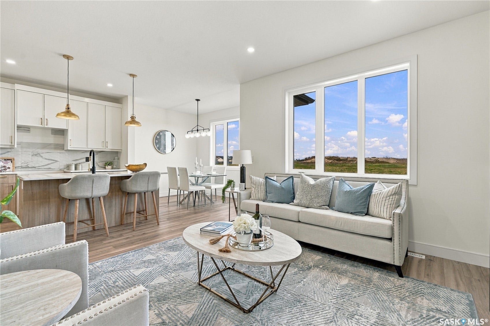 Open-concept living space with wood-finish flooring, white cabinetry, a kitchen island with seating, a dining area, and large windows