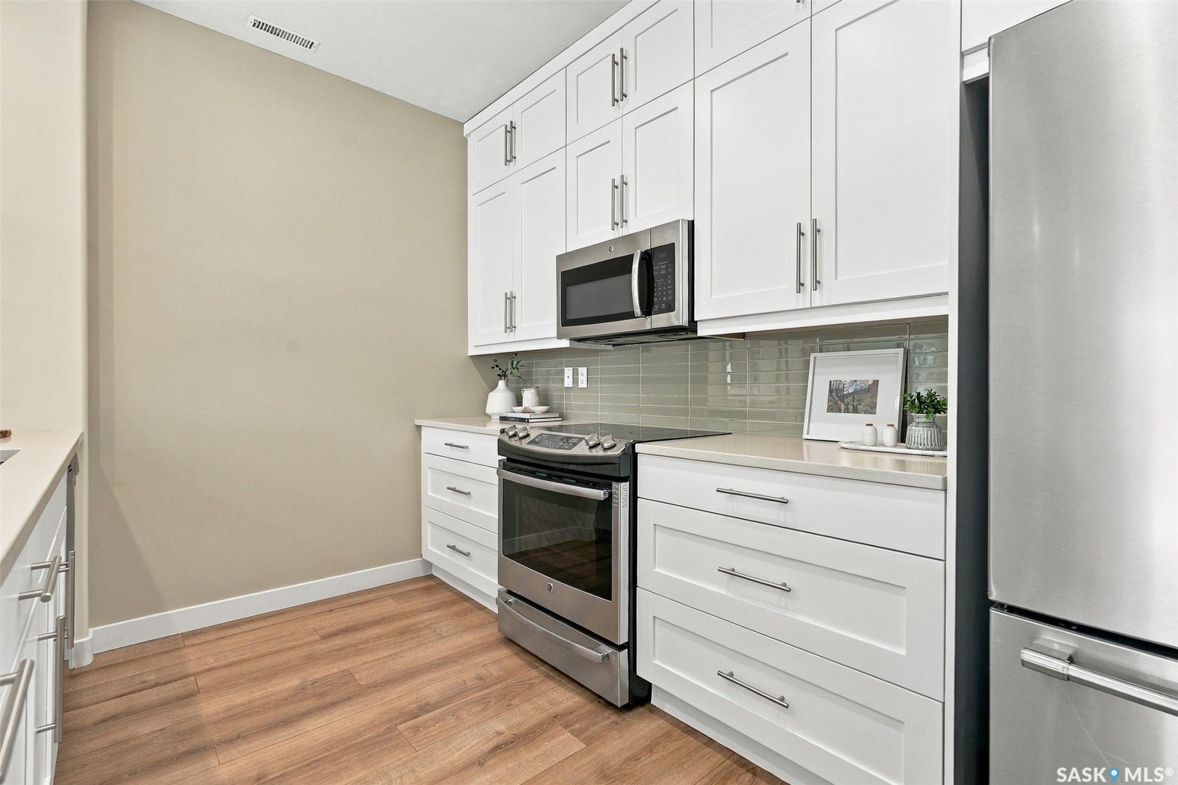 Modern kitchen featuring white shaker-style cabinetry, stainless steel appliances including a slide-in range and over-the-range microwave, subway tile backsplash, wood-finish flooring, and chrome hardware throughout