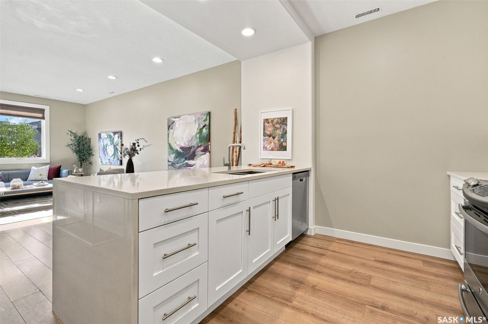 Kitchen island with white cabinetry, stainless steel sink, and light-toned countertop