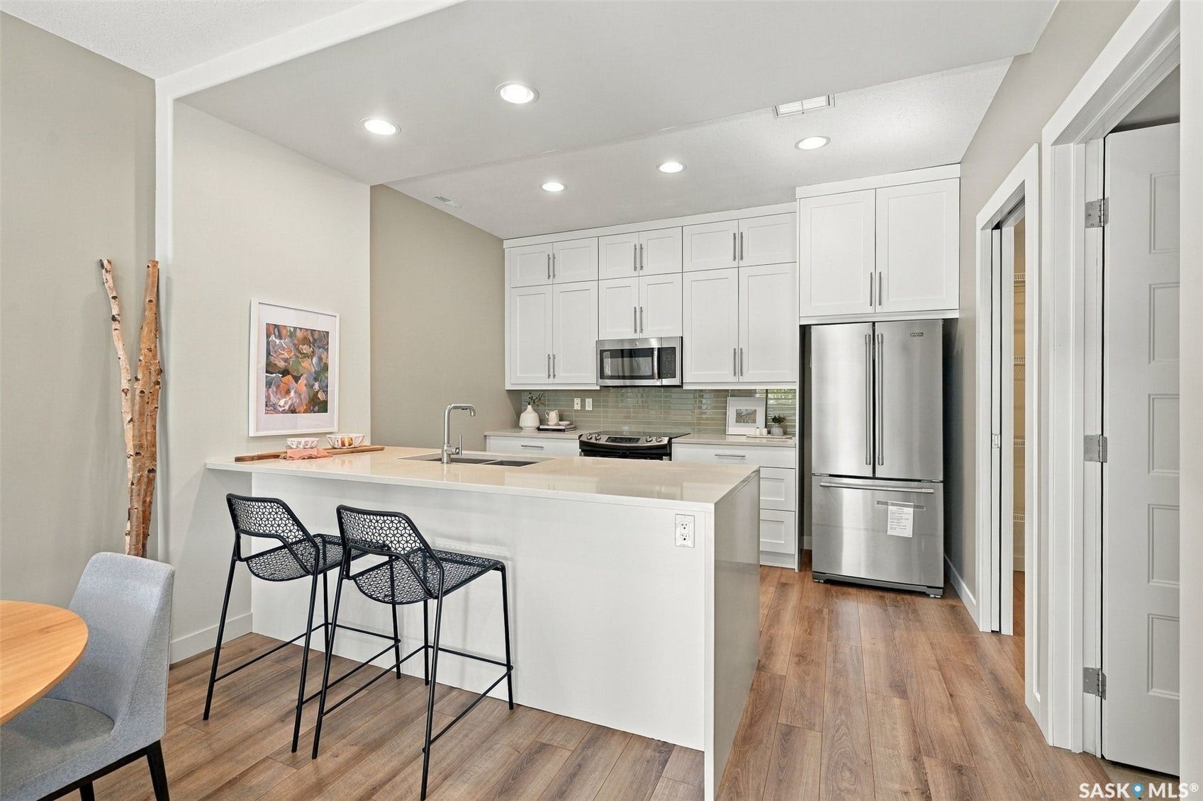 Modern kitchen featuring recessed lighting, stainless steel appliances, light-toned wood-finish flooring, white cabinetry, and a light-colored countertop with a built-in sink
