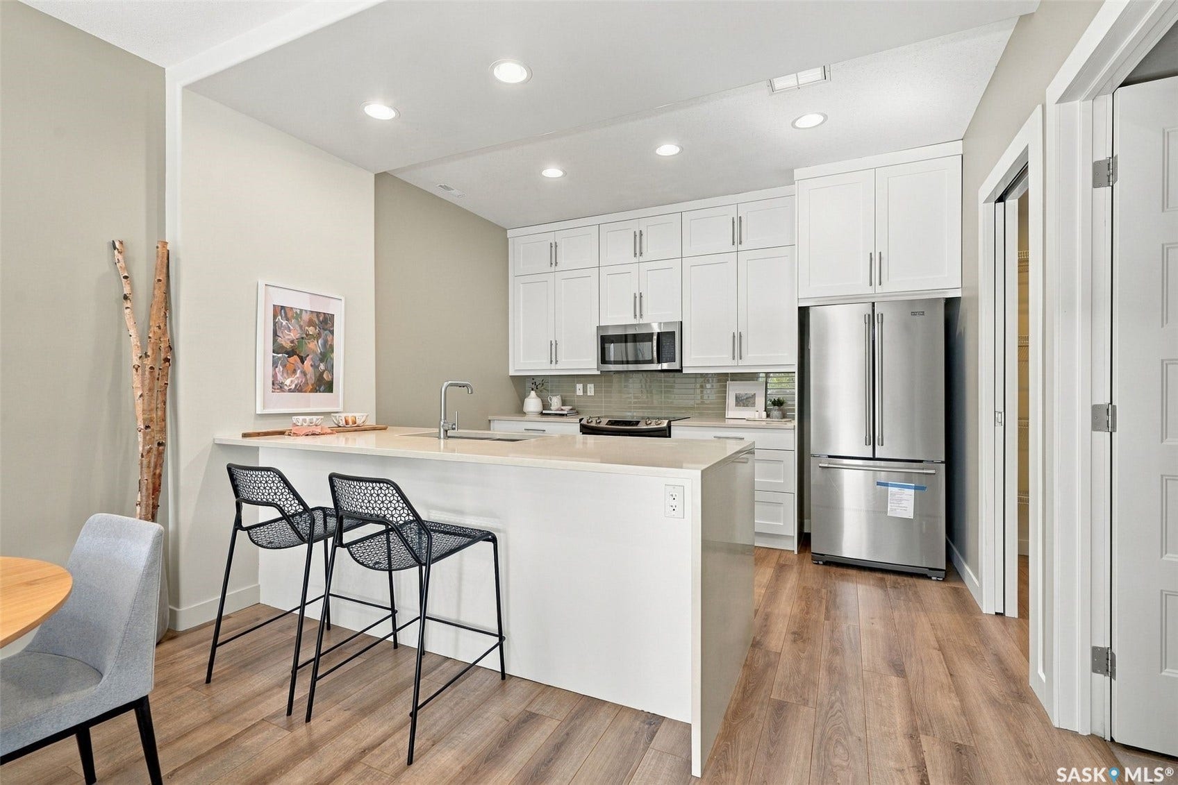 Kitchen featuring white cabinetry, integrated stainless steel appliances, a large island with seating, recessed lighting, and wood-finish flooring