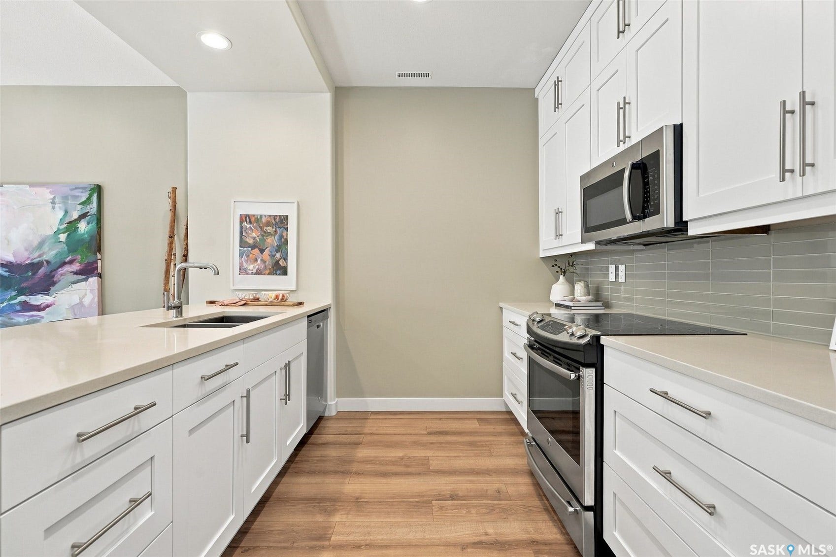 Modern kitchen featuring white shaker-style cabinetry, light-toned countertops, stainless steel appliances, a grey subway tile backsplash, and wood-finish flooring