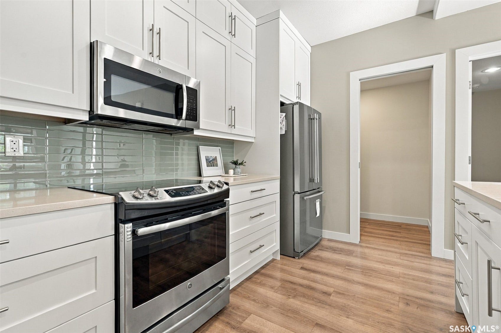 White shaker cabinetry with stainless steel hardware, stainless steel appliances, light-toned countertop, glass tile backsplash, and wood-finish flooring