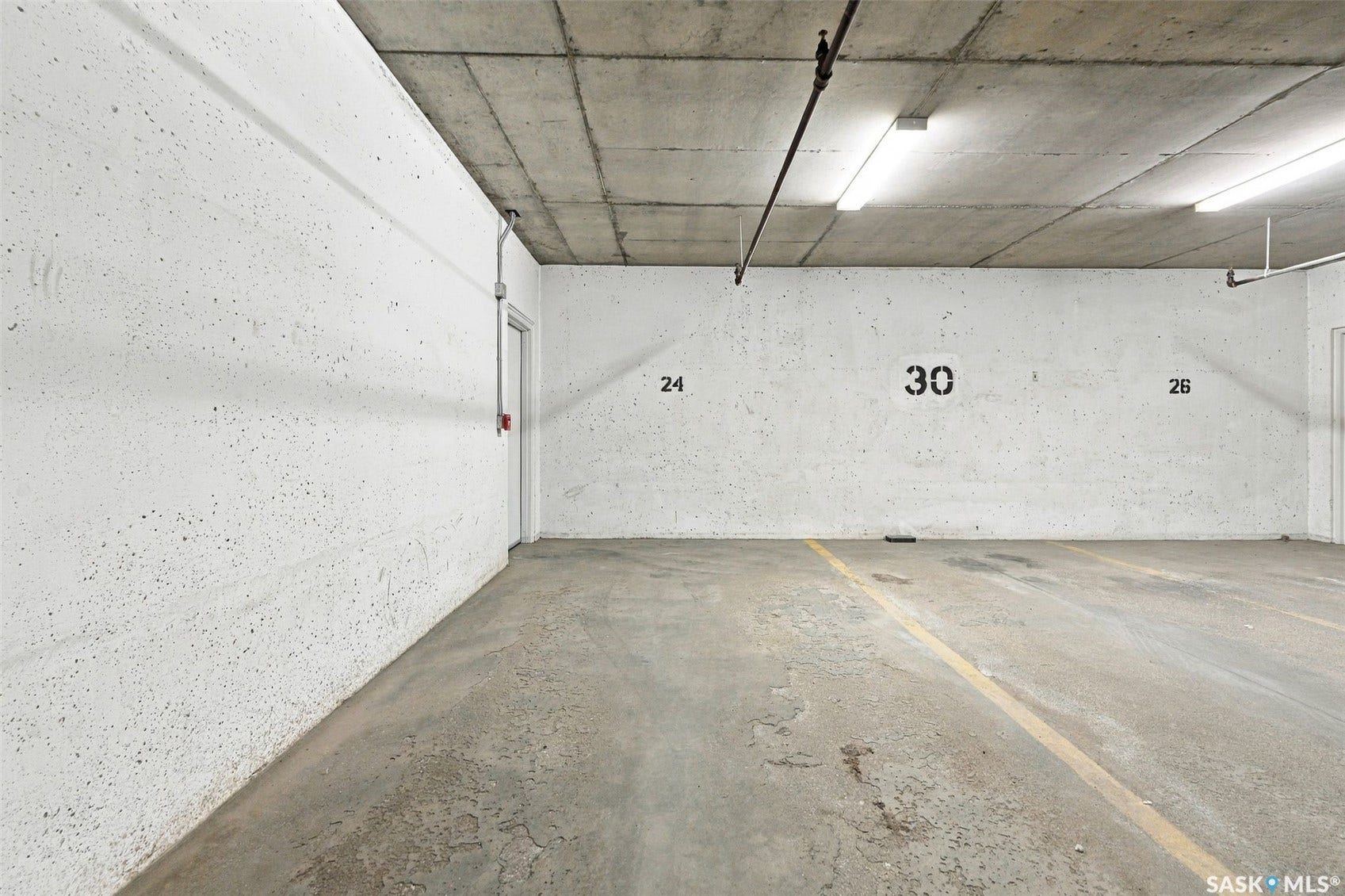 Concrete flooring with yellow parking lines, painted concrete walls, and overhead fluorescent lighting