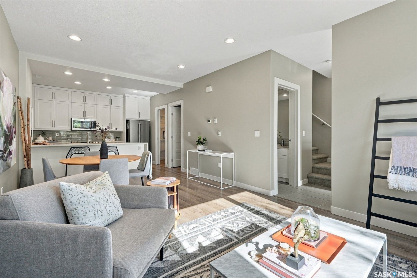 Open-concept living area with recessed lighting, wood-finish flooring, and a kitchen featuring white cabinetry, a large island, and stainless steel appliances