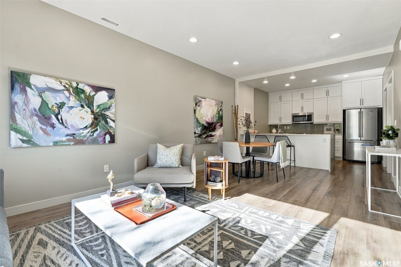 Open-concept living space with wood-finish flooring, recessed lighting, and a kitchen featuring white cabinetry, stainless steel appliances, and a breakfast bar
