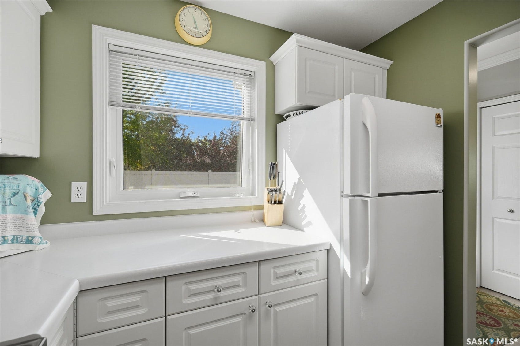 White cabinetry with crown molding, solid surface countertops, and a full-size refrigerator