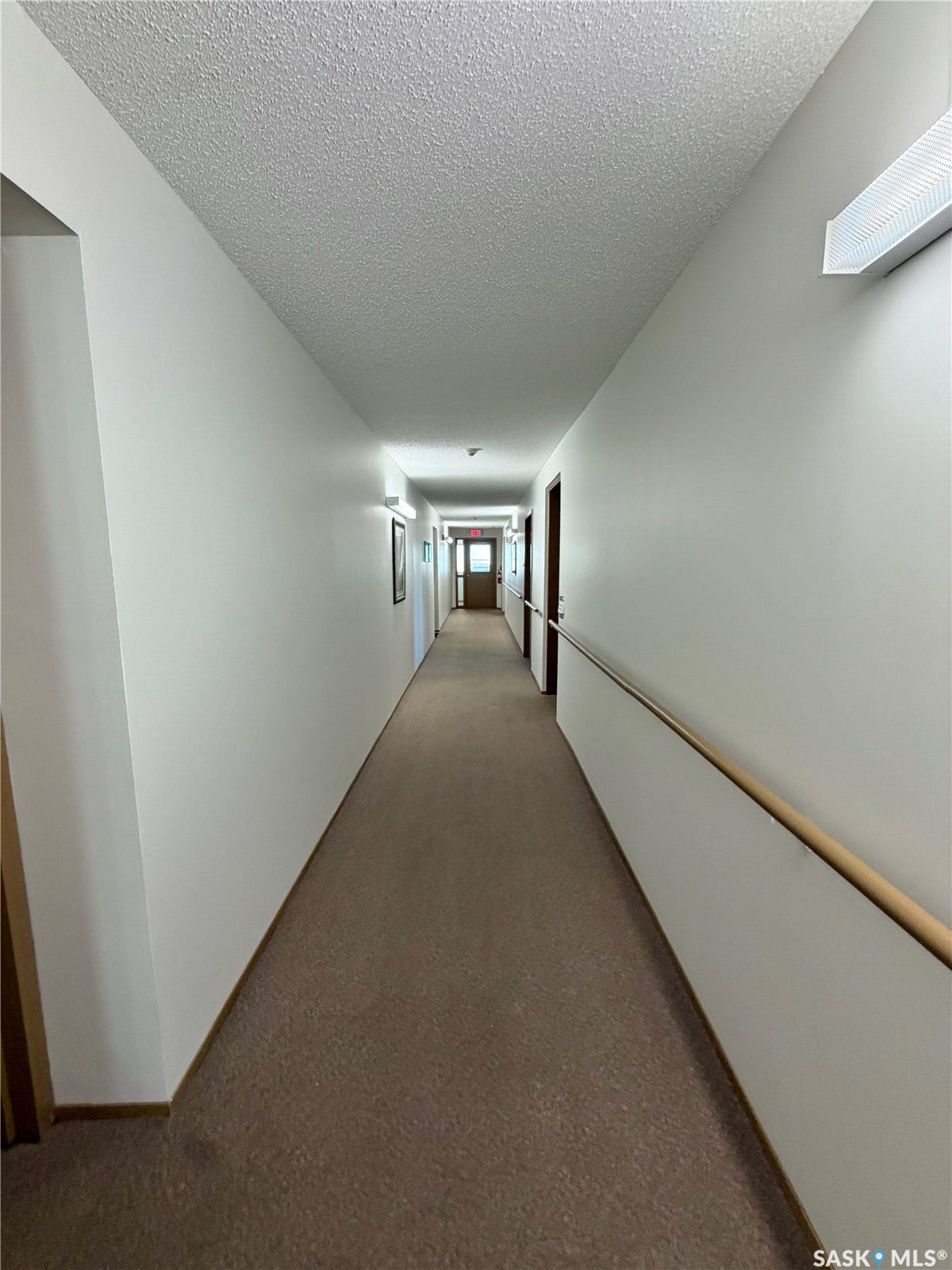 305 1st Street W, #301, Rosetown SK S0L 2V0 Long hallway with textured ceilings, wall-mounted lighting, and a continuous handrail