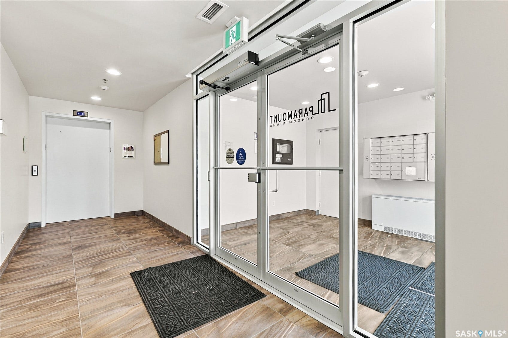 Building entrance featuring glass doors, wood-finish flooring, a wall-mounted mailbox system, and an elevator