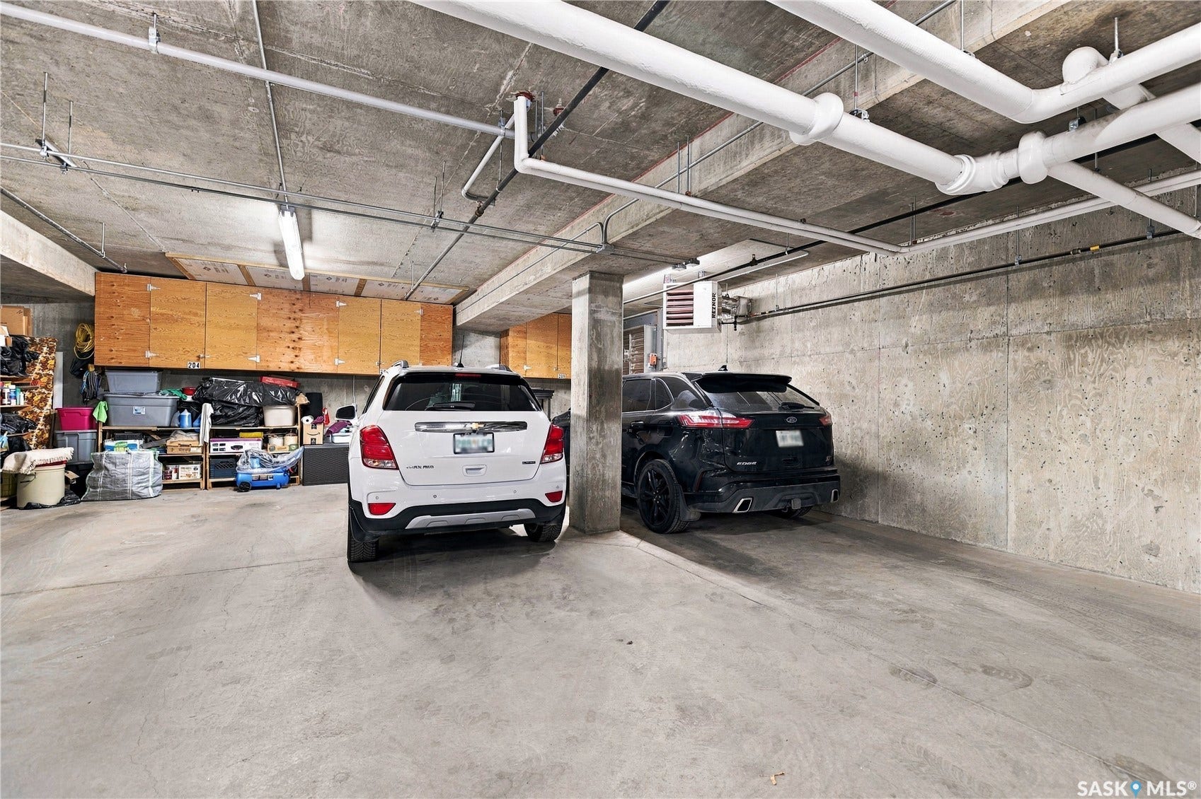 Concrete floor parking area with overhead piping and built-in storage cabinetry