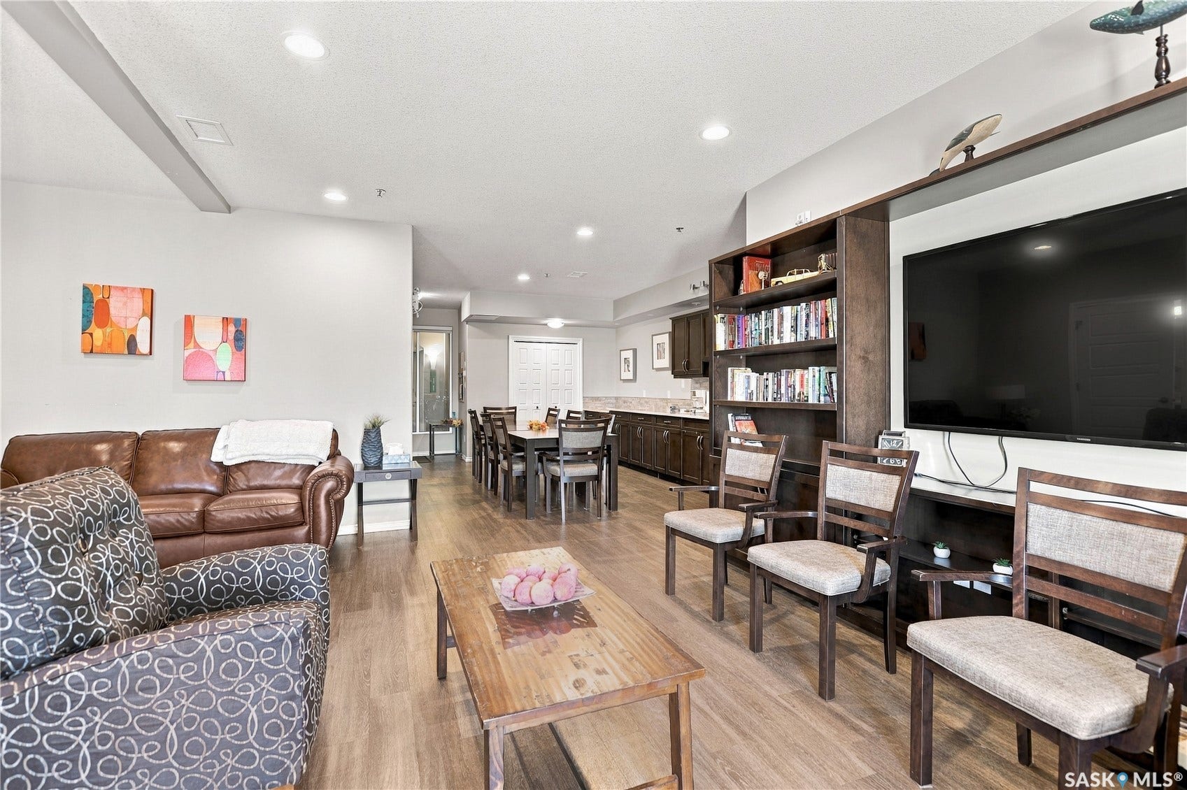 Recessed ceiling lighting, wood-finish flooring, built-in shelving, built-in media console, and a dining area with dark wood cabinetry