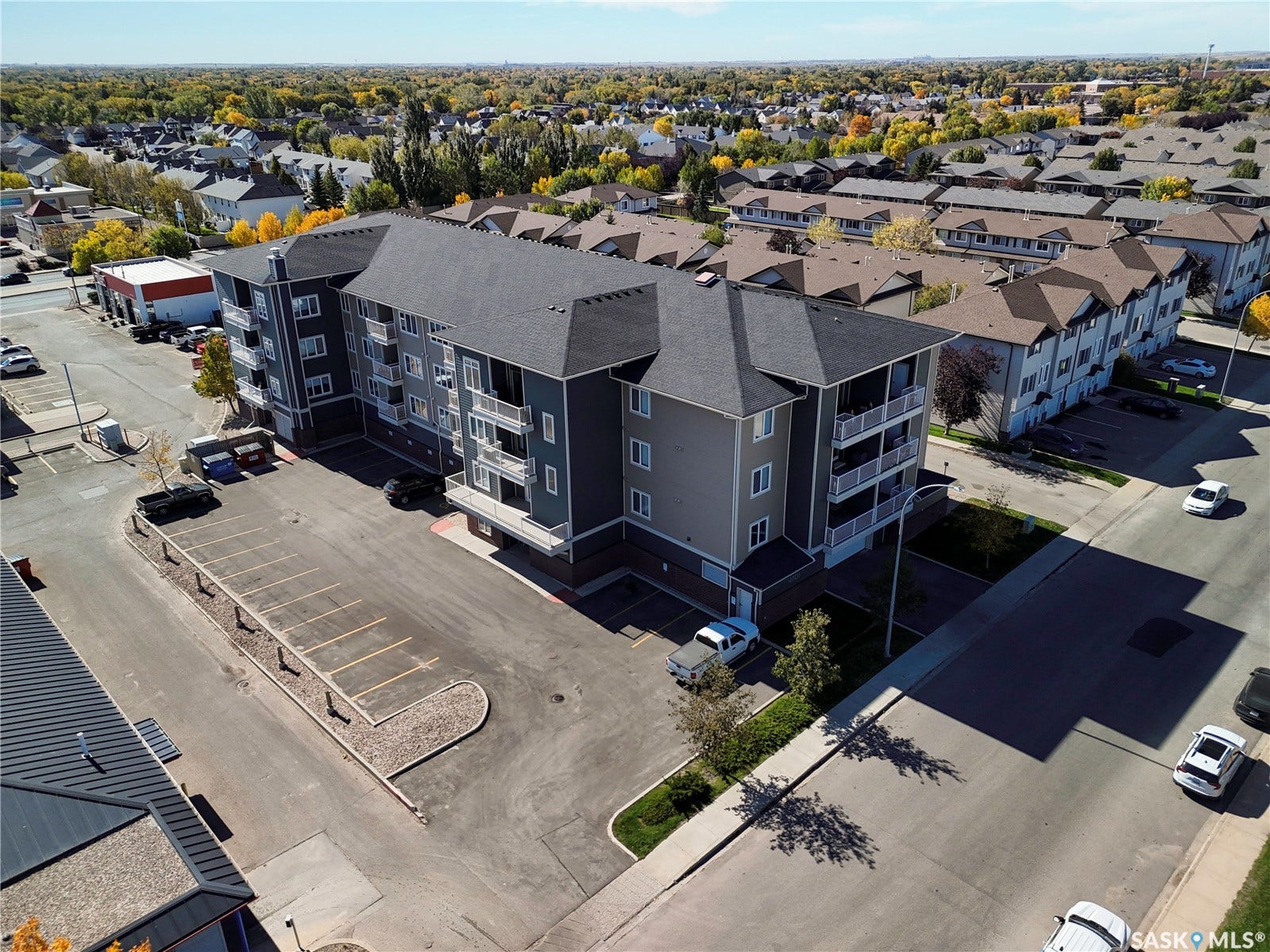 Multi-story apartment building with dark gray siding, multiple balconies, and an on-site surface parking lot