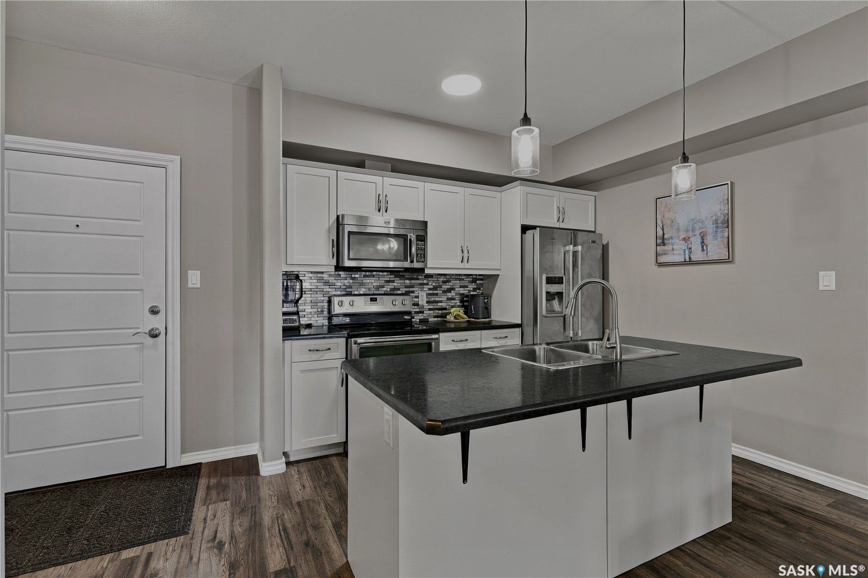 Modern kitchen featuring white cabinetry, stainless steel appliances including a gas range and refrigerator, black quartz countertops, a large island with seating, pendant lighting, and wood-finish flooring throughout