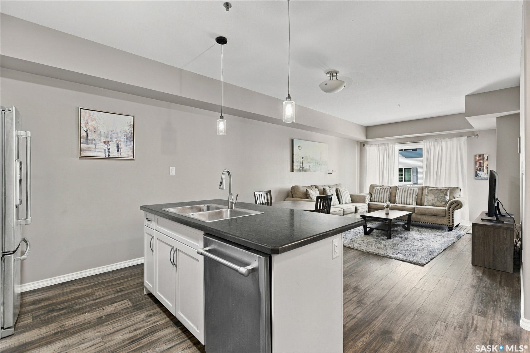 Wood-finish flooring, kitchen island with dual basin sink, stainless steel dishwasher, white cabinetry, and pendant lighting