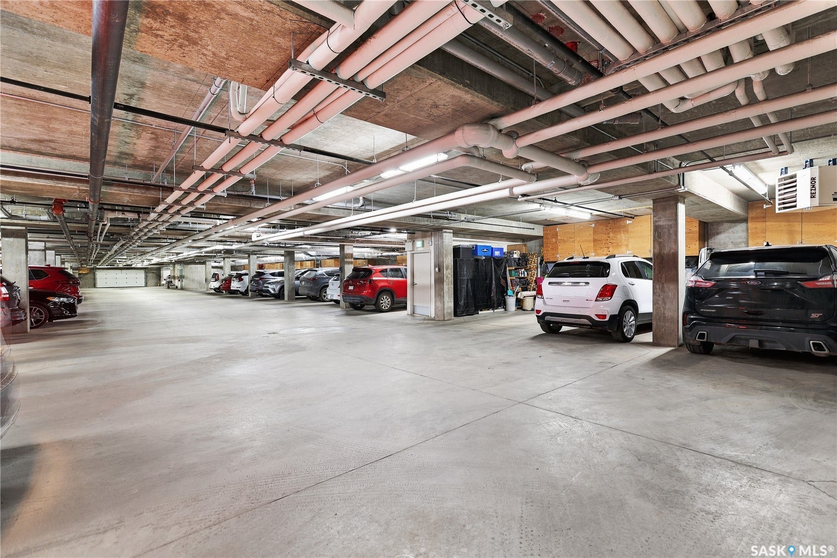Spacious underground parking facility with concrete flooring, exposed ceiling, and multiple fluorescent light fixtures