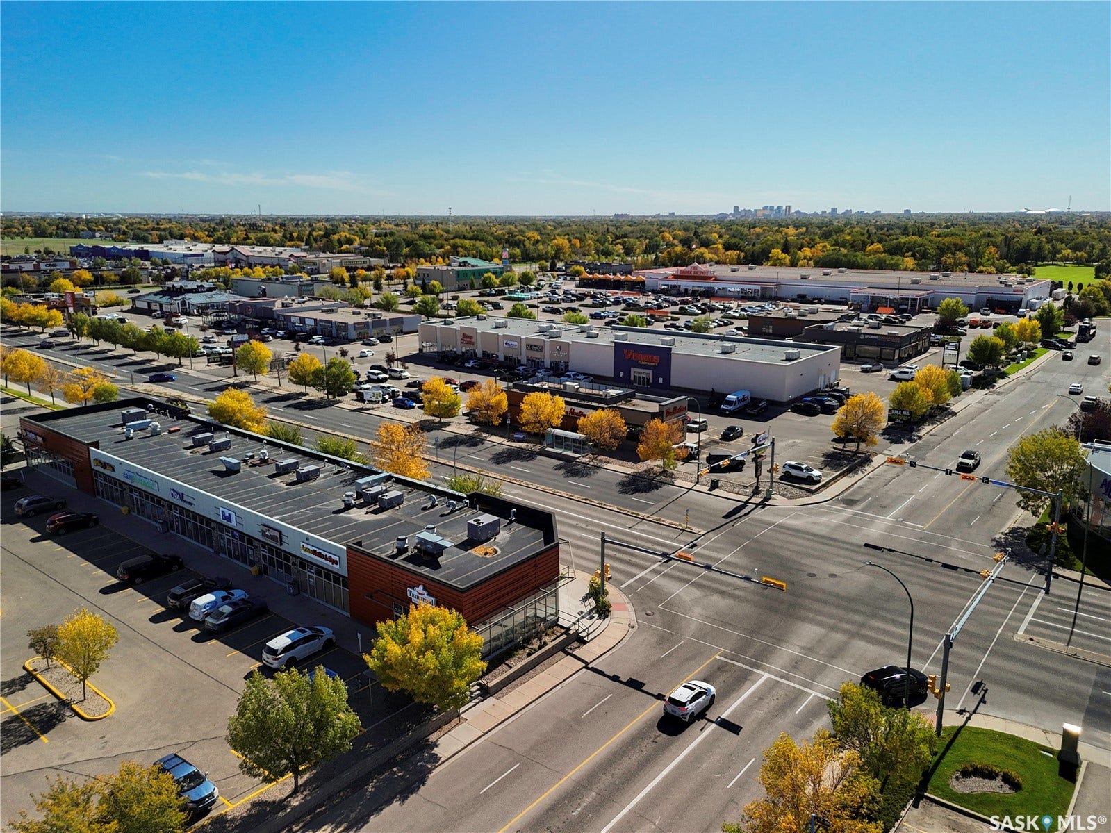 Commercial building with a flat roof, featuring multiple storefronts and an asphalt parking lot