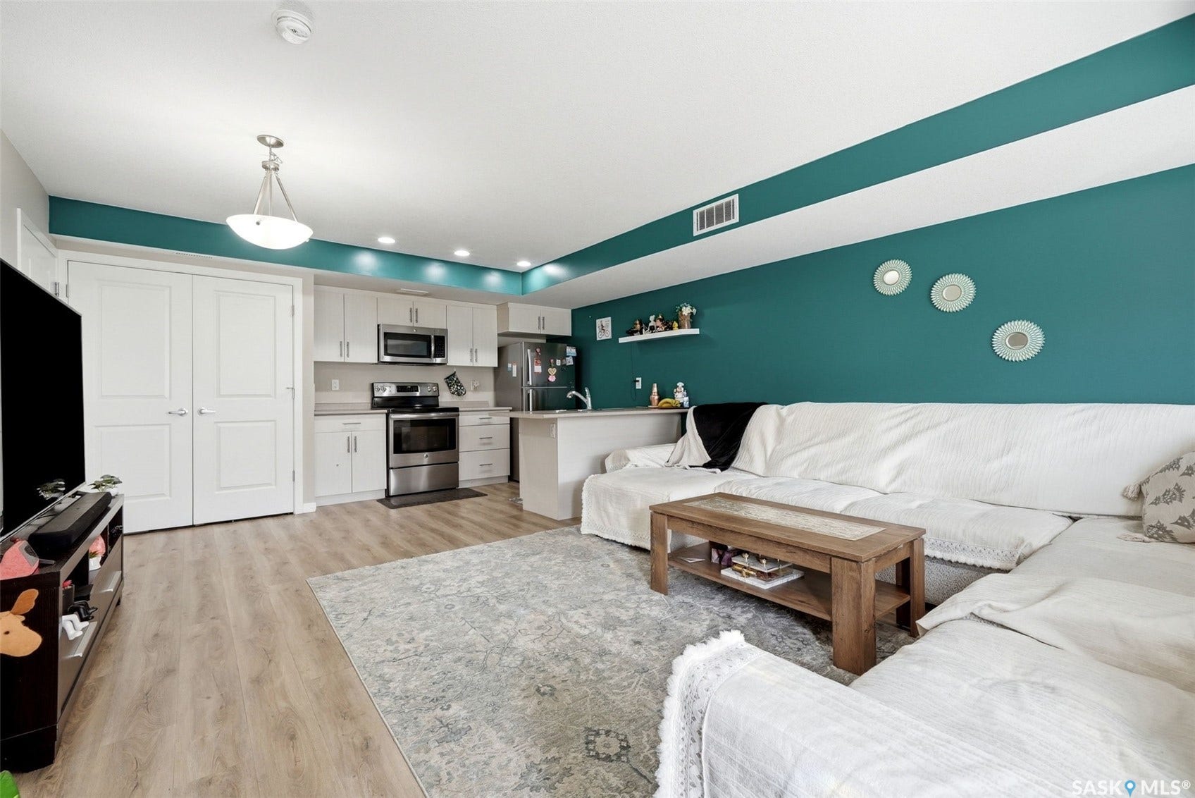 Wood-finish flooring, recessed lighting, and a kitchen featuring stainless steel appliances, light cabinetry, and a peninsula with countertop space