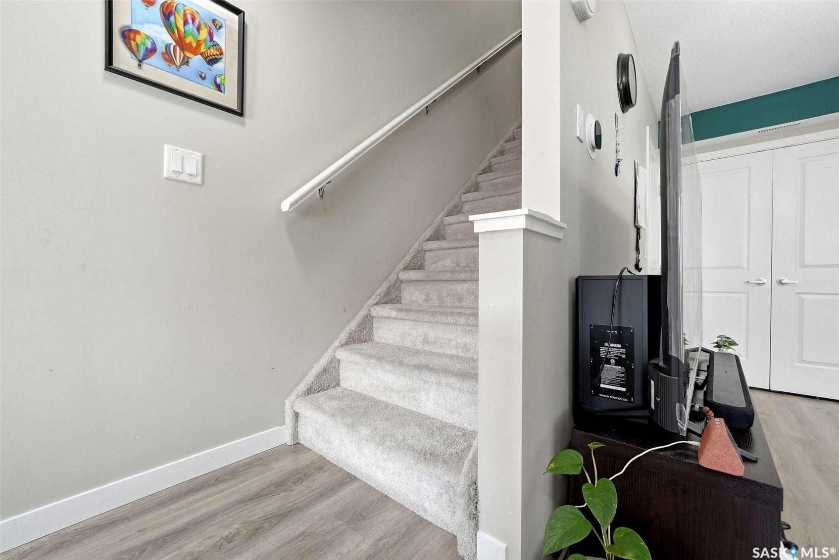 Bright entryway featuring a floating staircase with metal handrail, wood-finish plank flooring, and neutral wall palette