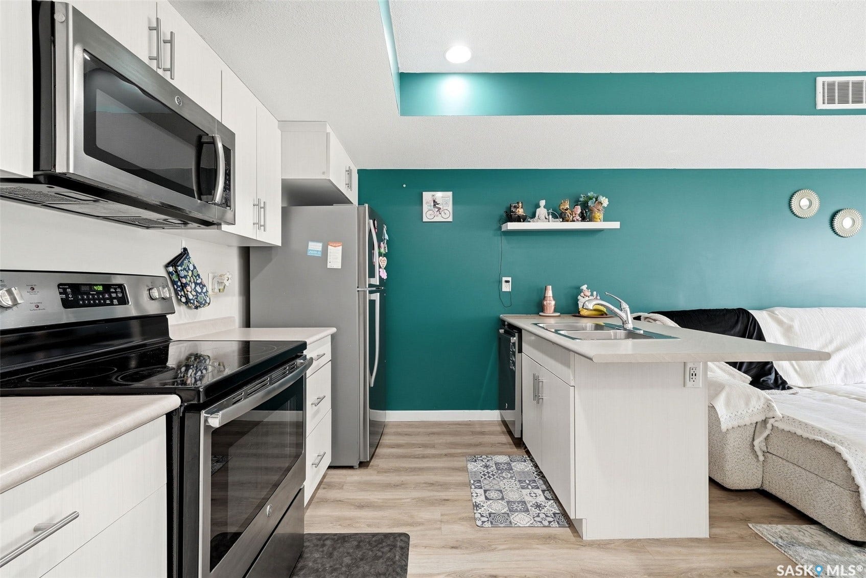 Kitchen featuring white cabinetry, stainless steel appliances, wood-finish flooring, and a peninsula with an integrated sink
