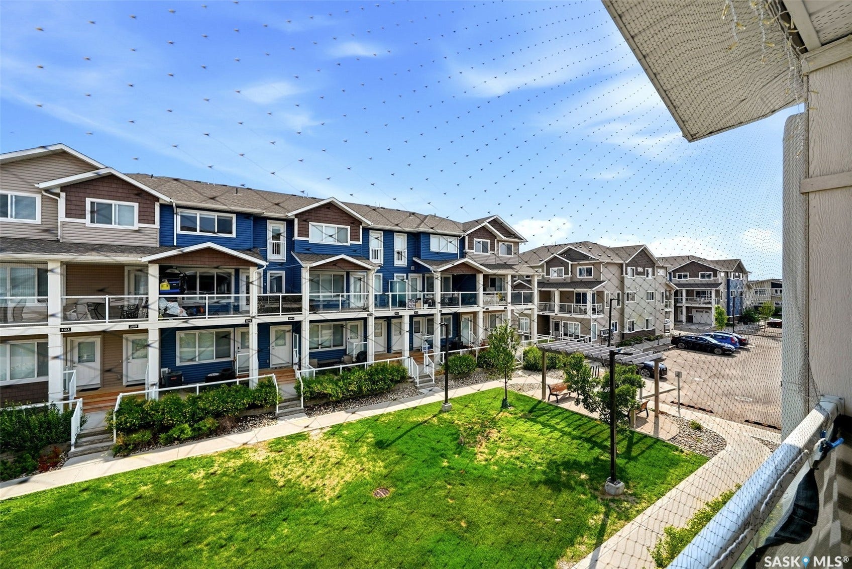 Townhome exterior with a dedicated green space, balconies with glass railings, and private patio areas