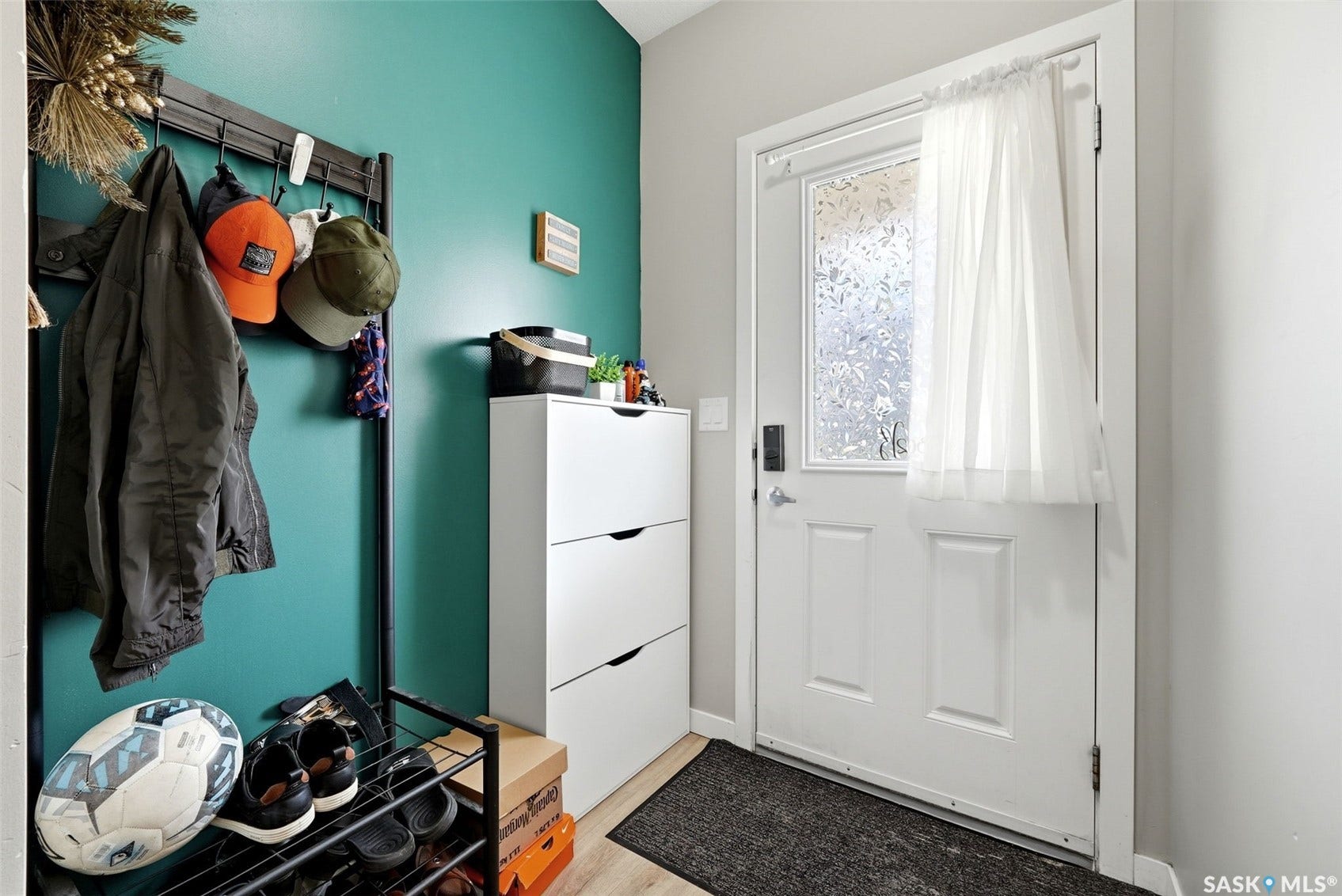 Welcoming entryway featuring a vibrant turquoise accent wall, white six-panel entry door with sidelights, white modular storage cabinetry with drawers, dark tile flooring, and wall-mounted hooks and rod for organized coat and accessory storage