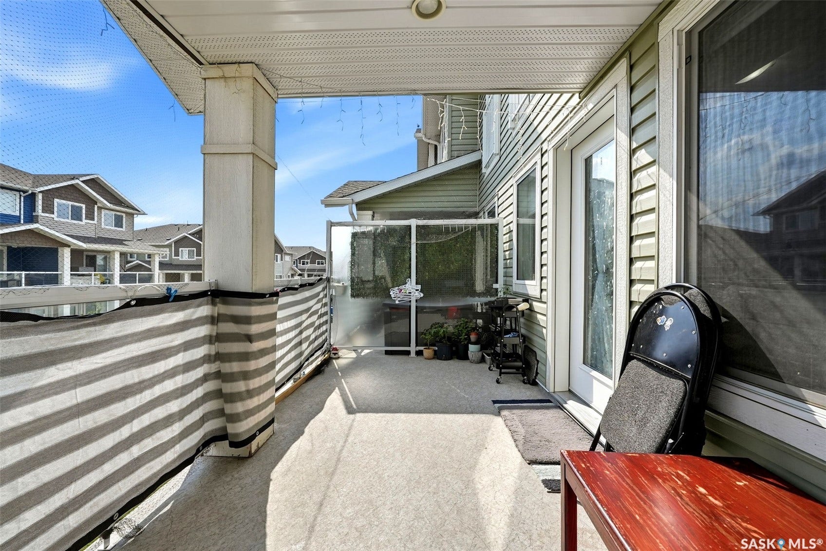 Covered balcony with concrete flooring, supported by a substantial column, featuring a glass panel partition and direct access via a white-framed door