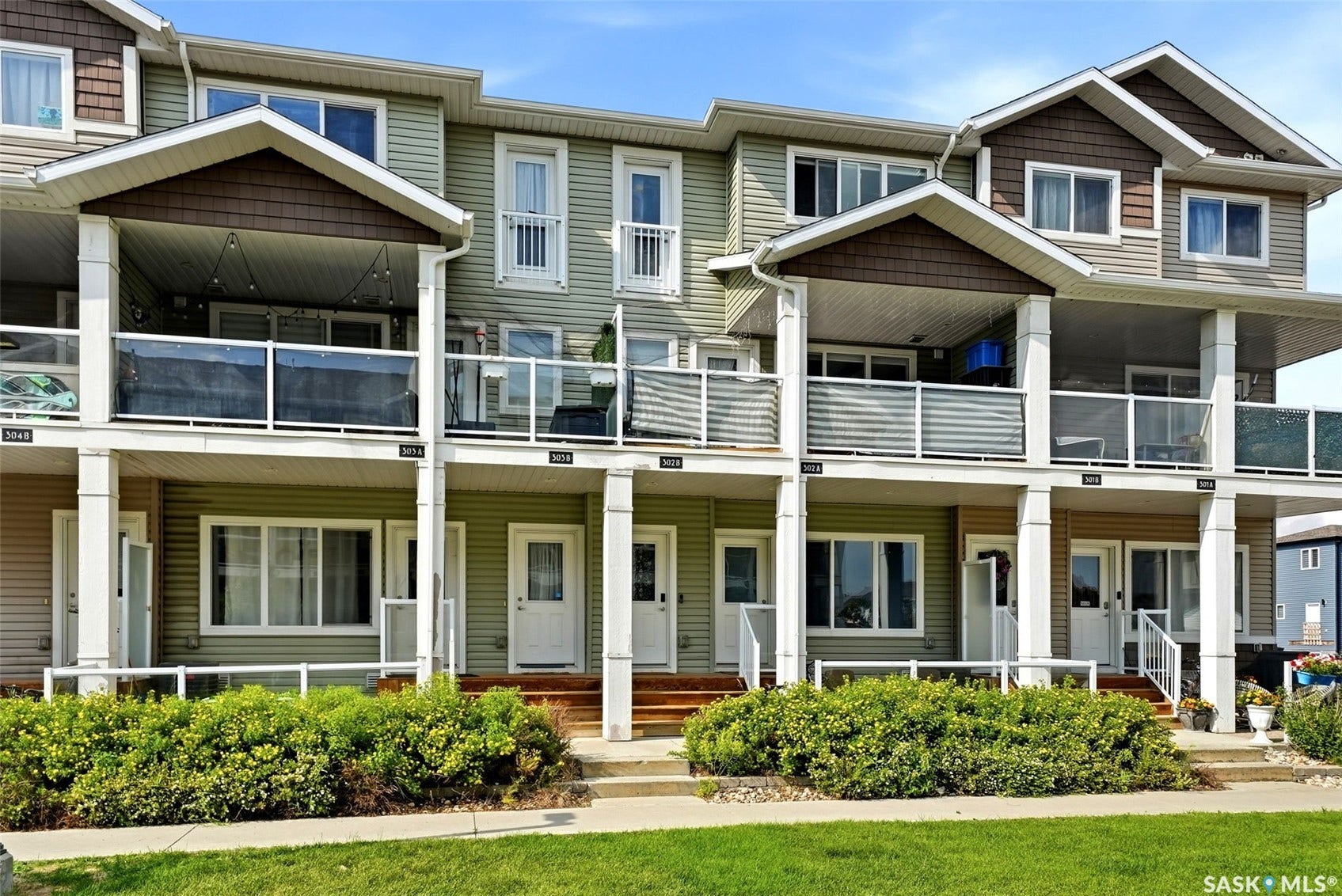 Townhome exterior featuring multiple balconies with glass railings, covered entryways, and varied siding finishes