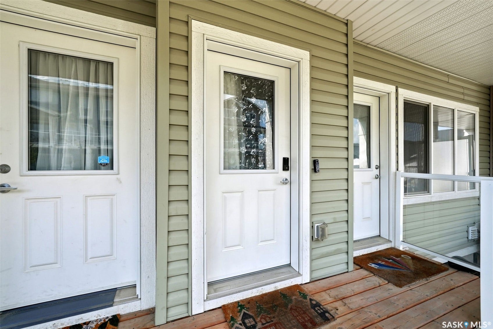 Wood-finish flooring on the porch, featuring multiple entry doors with glass inserts and light green horizontal siding