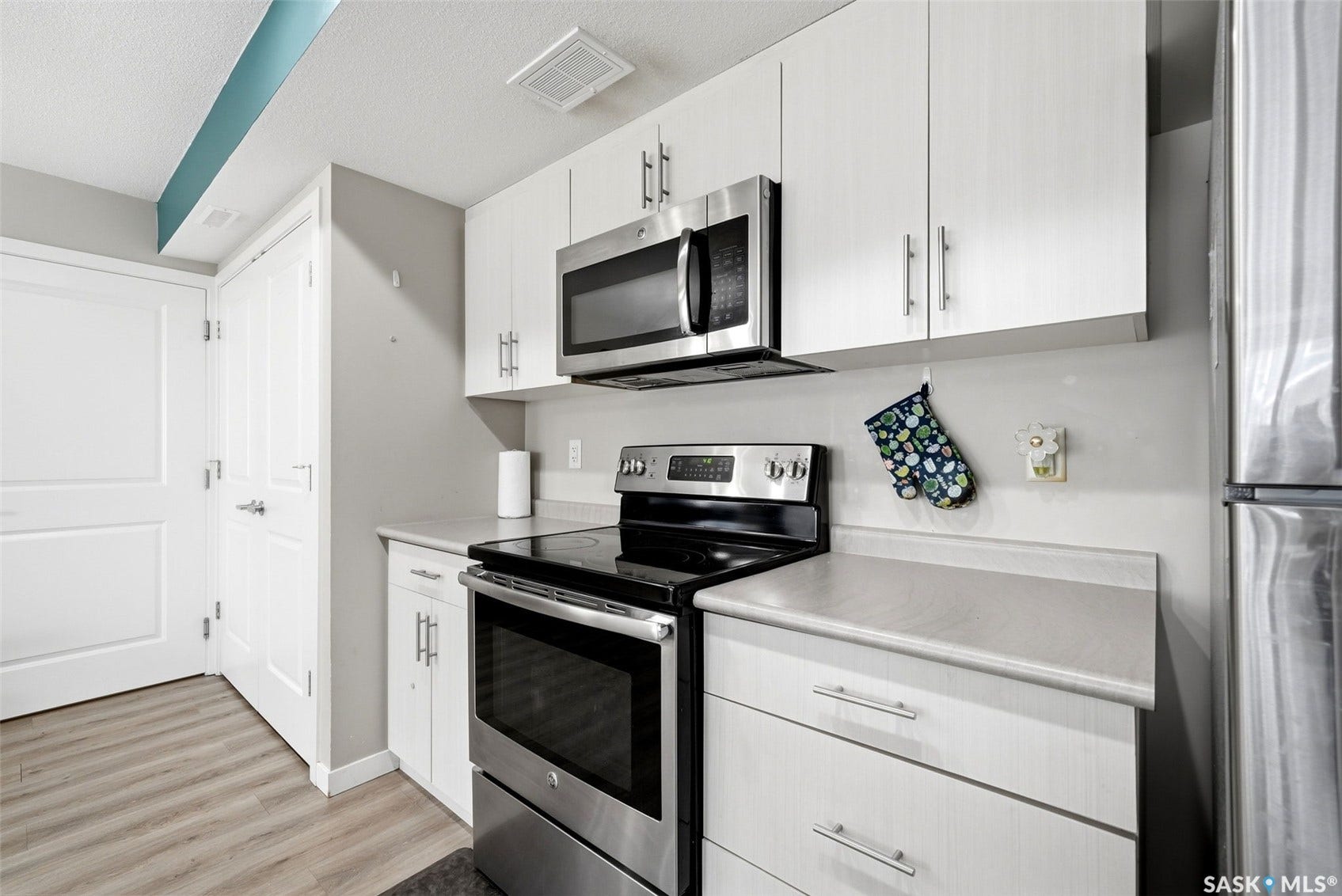 Kitchen featuring wood-finish flooring, white cabinetry with brushed nickel hardware, stainless steel appliances, and light-toned countertops