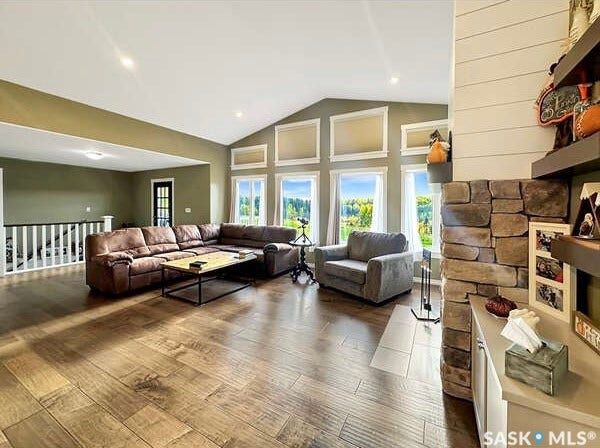Vaulted ceiling, wood-finish flooring, multiple windows, stone-front fireplace, and recessed lighting