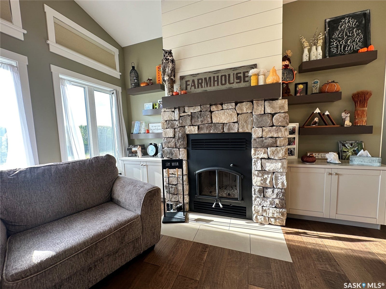 Stacked stone fireplace with a dark wood mantel, wood-finish flooring, and built-in floating shelves
