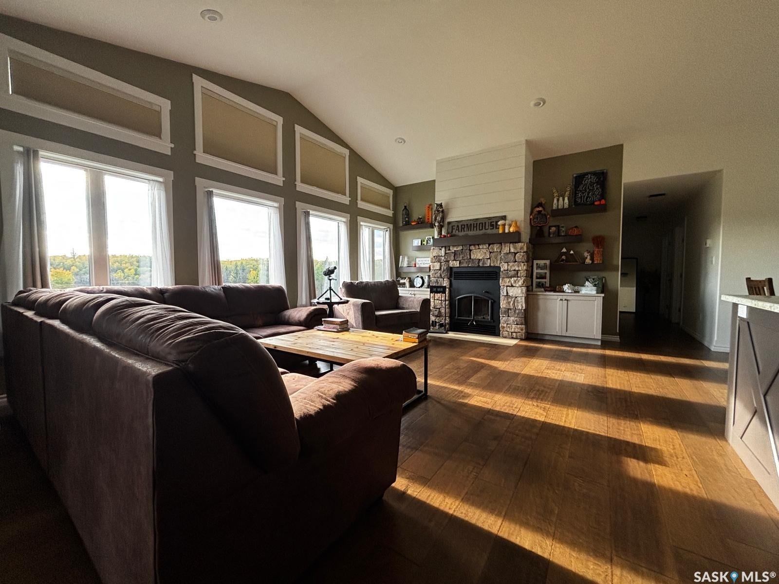Vaulted ceiling with recessed lighting, stone-clad fireplace, wood-finish flooring, built-in shelving, and multiple windows