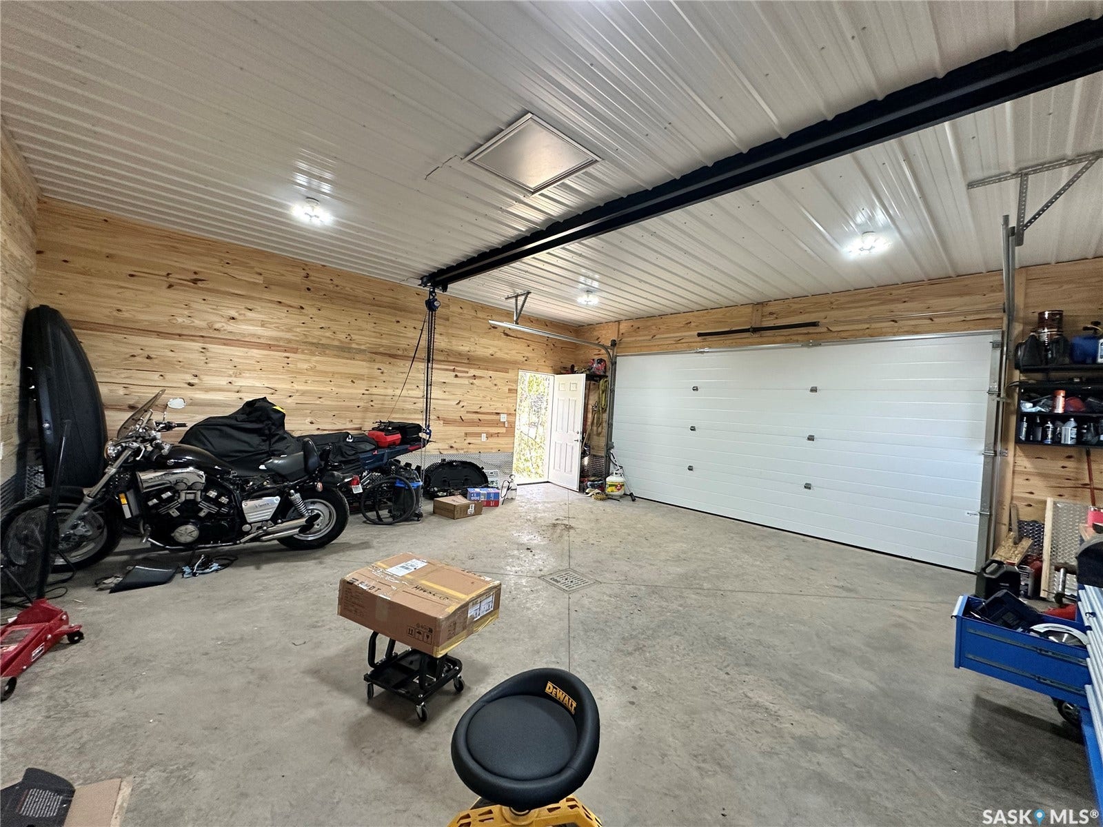Concrete flooring, wood-paneled walls, white paneled garage door, and white paneled ceiling