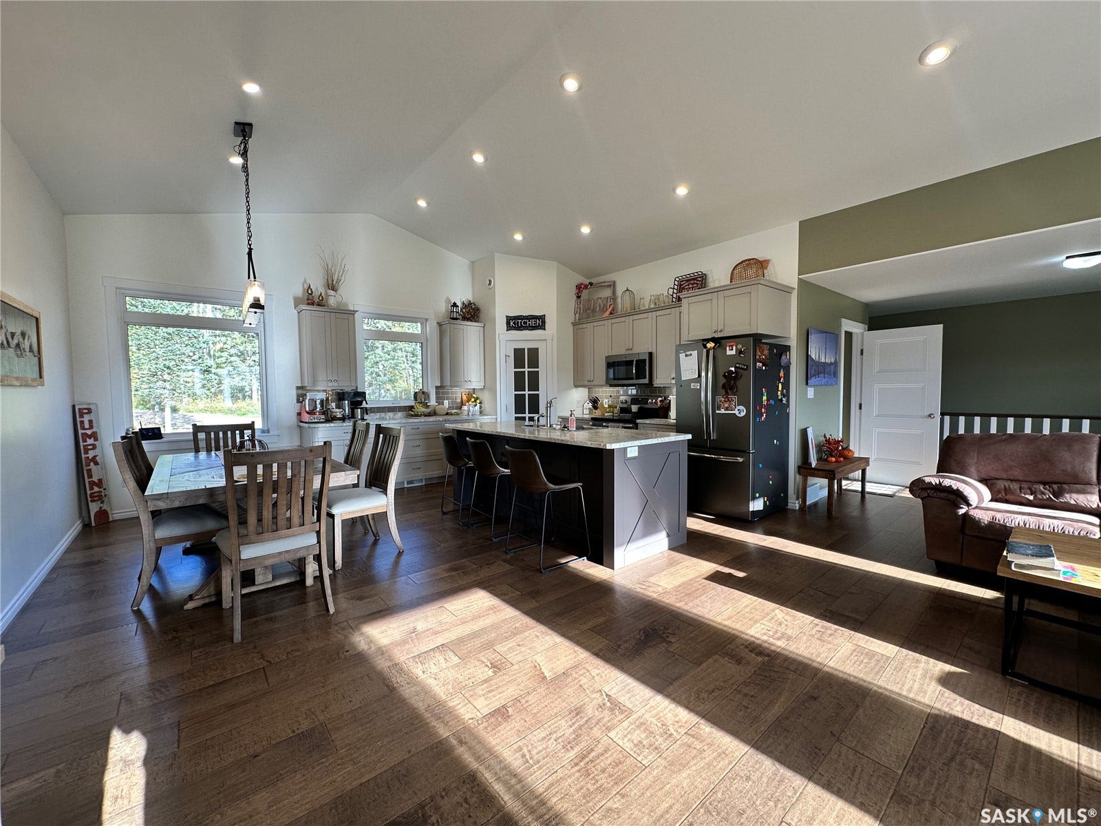 Vaulted ceiling with recessed lighting, wood-finish flooring, kitchen island with seating, stainless steel appliances, and white shaker-style cabinetry