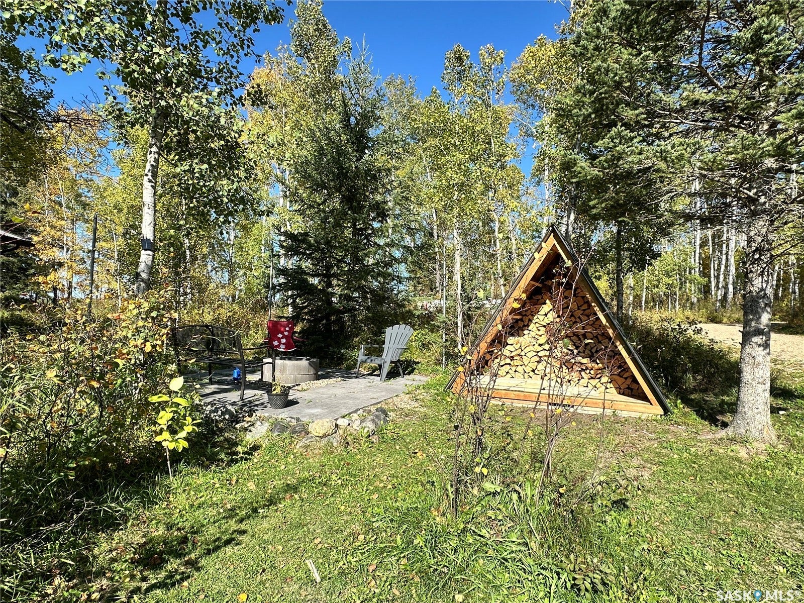 Wood-framed A-frame structure, concrete patio firepit close to the home, and mature trees surrounding
