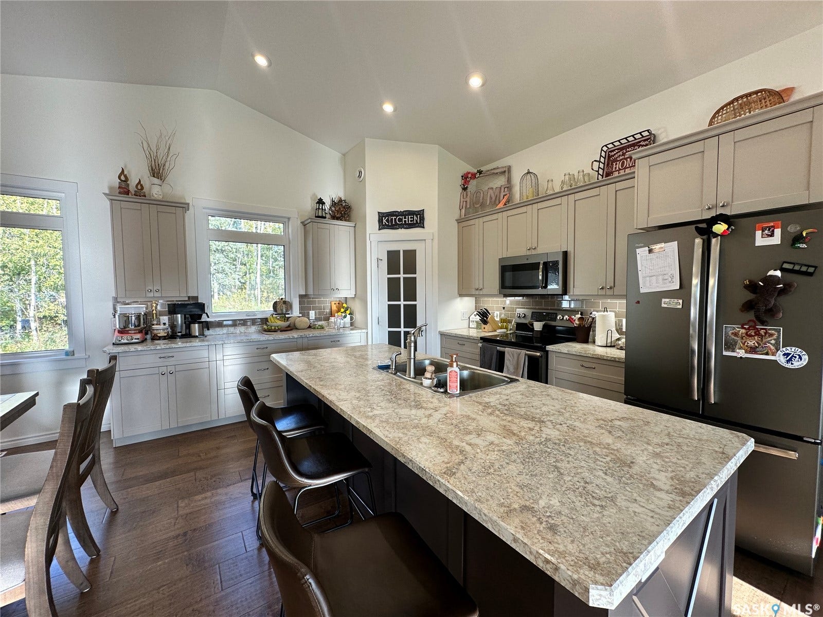 Vaulted ceiling kitchen featuring a large island with an undermount sink, wood-finish flooring, recessed lighting, and light-toned cabinetry