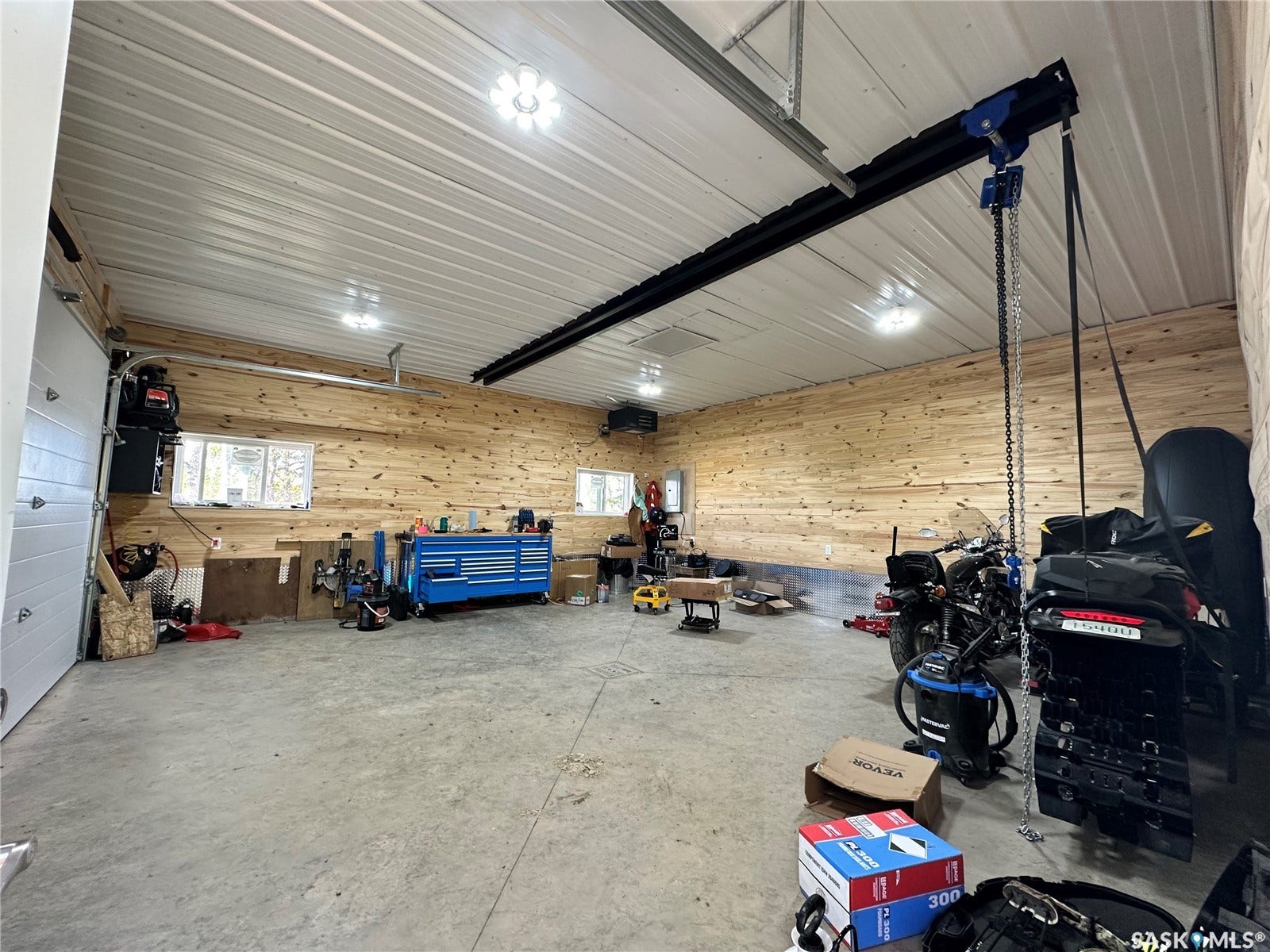 Garage space featuring a white corrugated ceiling, natural wood-paneled walls, concrete flooring, and multiple ceiling-mounted light fixtures