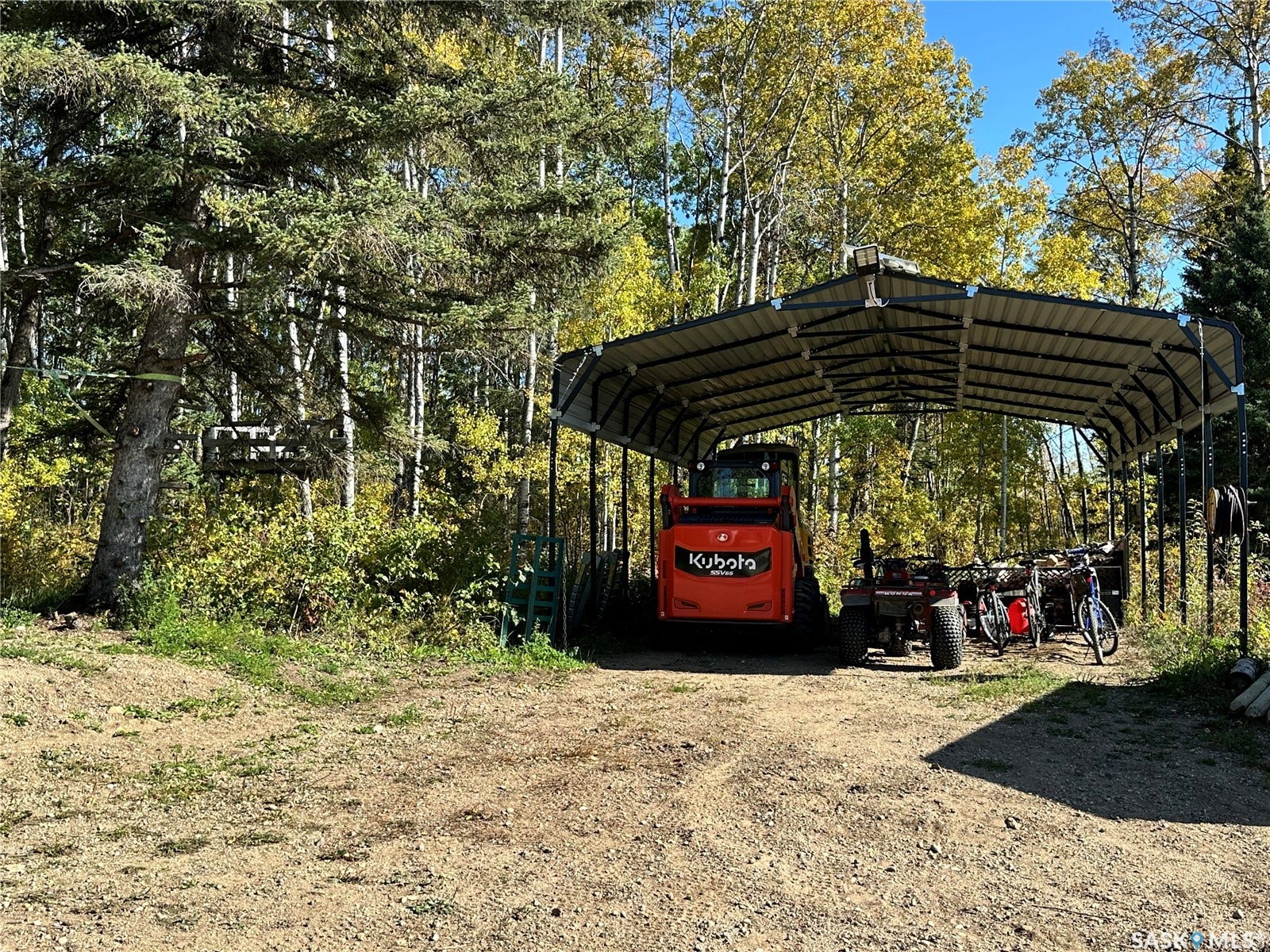 Metal-framed carport structure with a corrugated roof, situated on a gravel surface