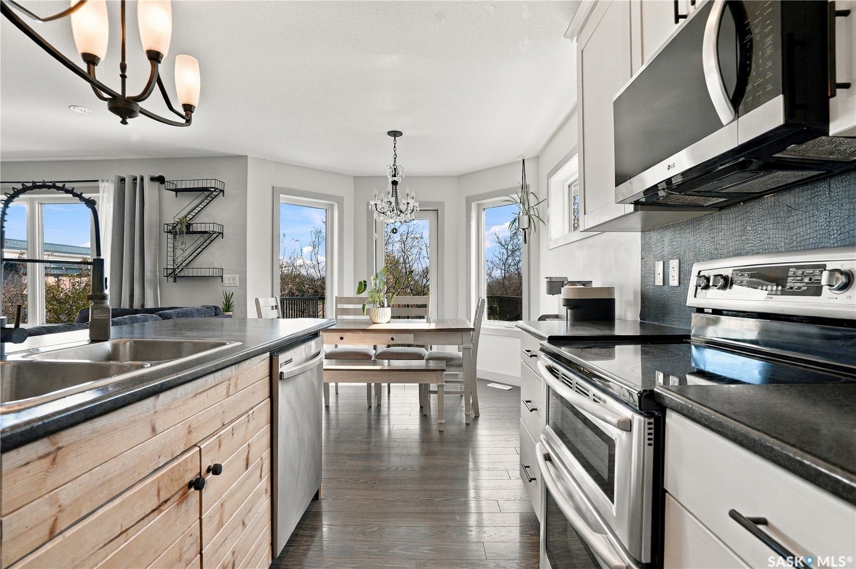 Kitchen featuring wood-finish island cabinetry, stainless steel appliances, dark countertops, and pendant lighting